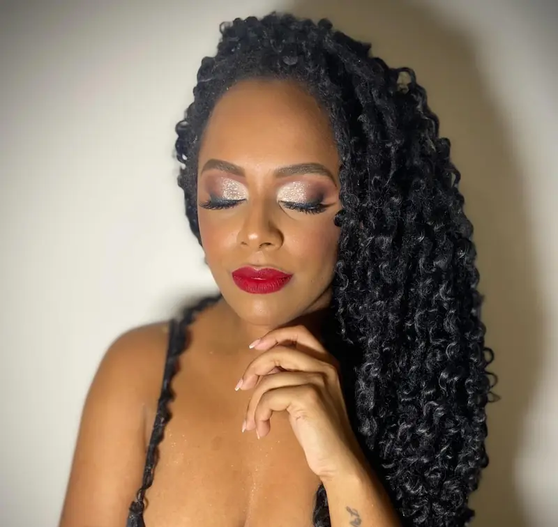 Close de cliente de olhos fechados com sombra cintilante, cílios marcados e batom vermelho, cabelo cacheado